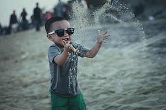 Happy toddler boy throwing sand at the beach wearing sunglasses