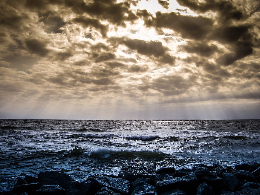 Dramatic Seascape with Sunbeams Breaking Through Clouds Over Rocky Shore