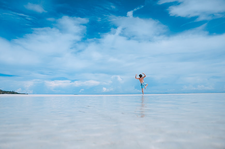 Man jumping on white sand beach under blue sky