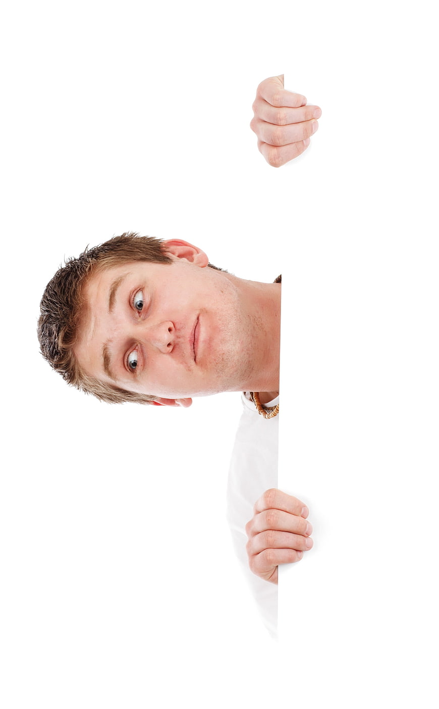 Young man peeking around white blank sign with copyspace