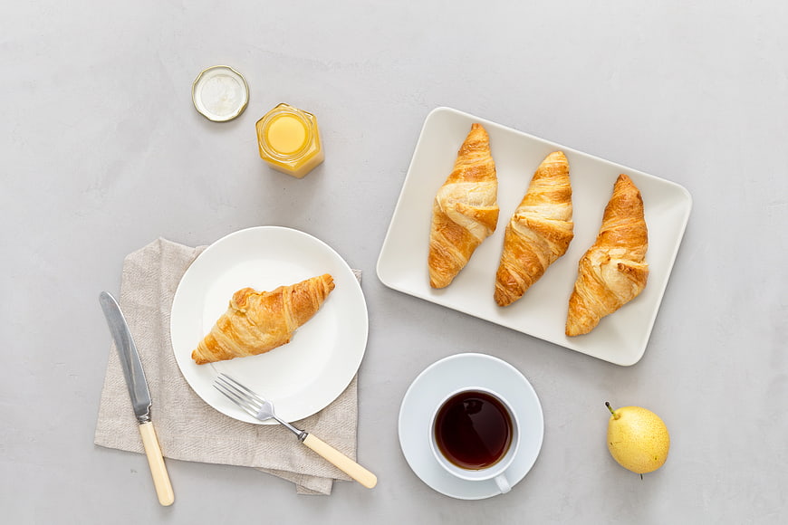 Top view of croissants, tea, and breakfast spread on gray background