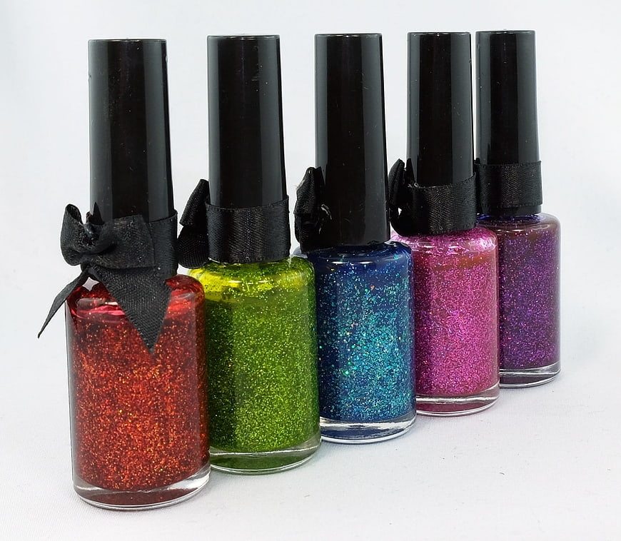 Five Glitter Nail Polish Bottles With Black Caps And Ribbons