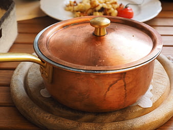 Copper cooking pot with lid on wooden board