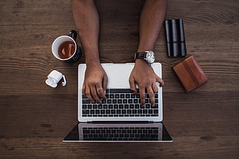 Top view of hands typing on laptop with coffee and accessories