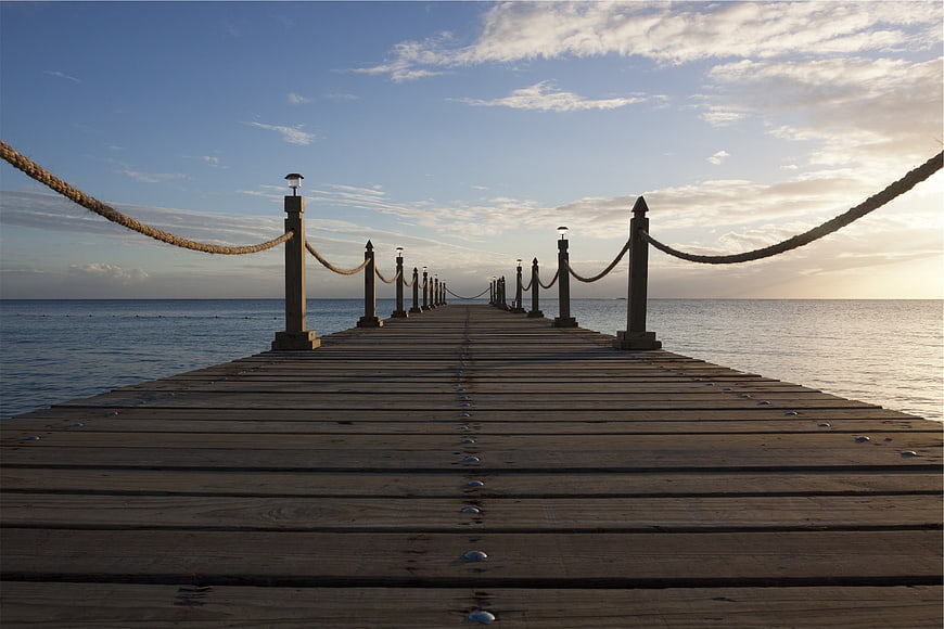 Wooden pier extending into calm ocean at sunset