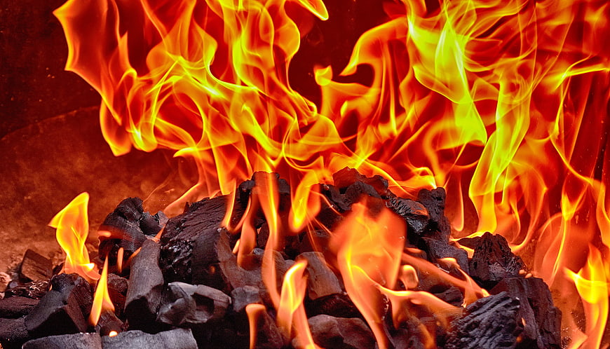 Close-up of burning charcoal briquettes with bright orange and yellow flames