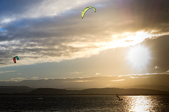 Kite surfers gliding on water during a dramatic sunset