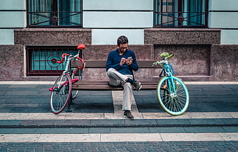 Man sitting on bench using smartphone between two colorful bicycles