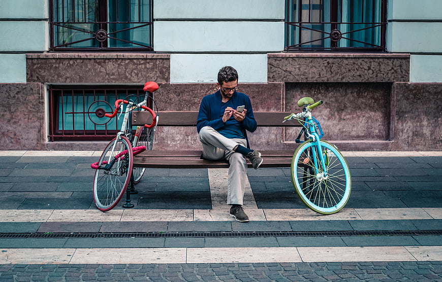 Man sitting on bench using smartphone between two colorful bicycles
