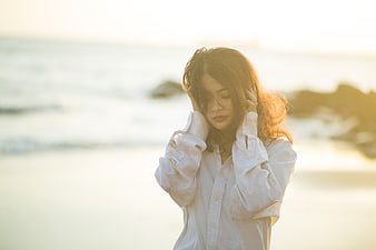 Melancholic woman in white shirt standing on beach at sunset