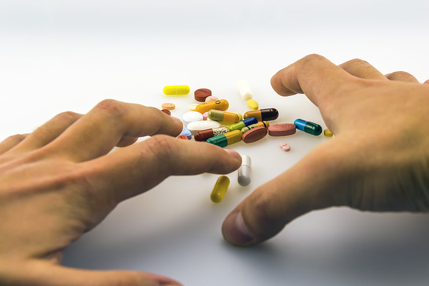 Hands Reaching for Scattered Pills and Capsules on White Background