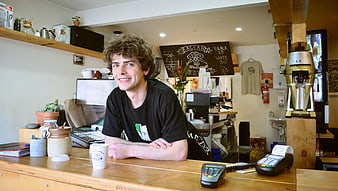 Smiling young man leaning on wooden counter in specialty coffee shop