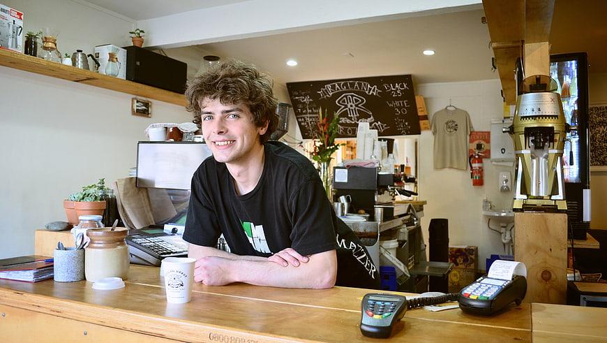 Smiling young man leaning on wooden counter in specialty coffee shop