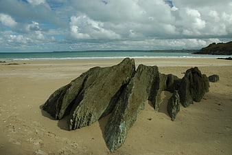 Dramatic rock formation on sandy beach with ocean and clouds