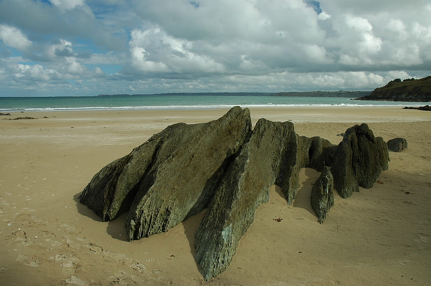 Dramatic rock formation on sandy beach with ocean and clouds