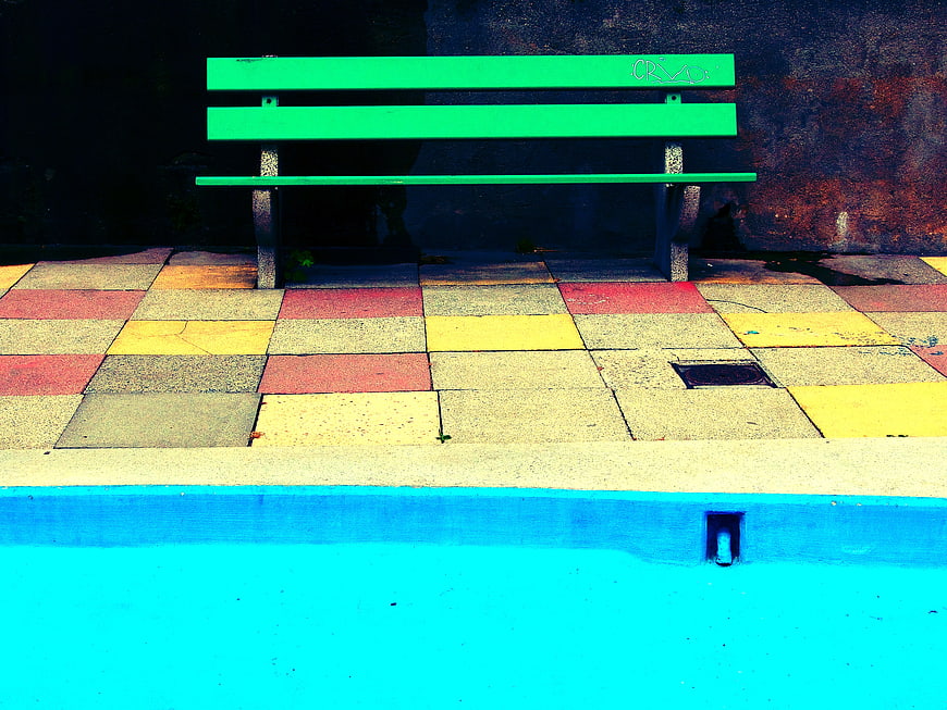 Vibrant Green Bench on Colorful Tiles Near Blue Pool