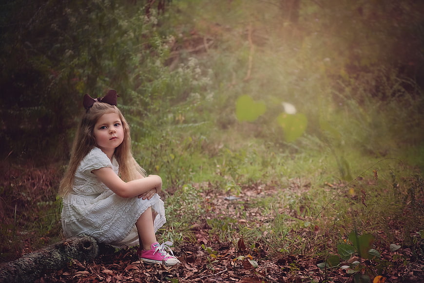 Young girl sitting on a log in a misty forest