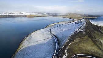 Aerial view of winding road along snowy mountain ridge and lake