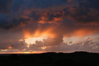 Dramatic sunset with sun rays breaking through clouds over dunes