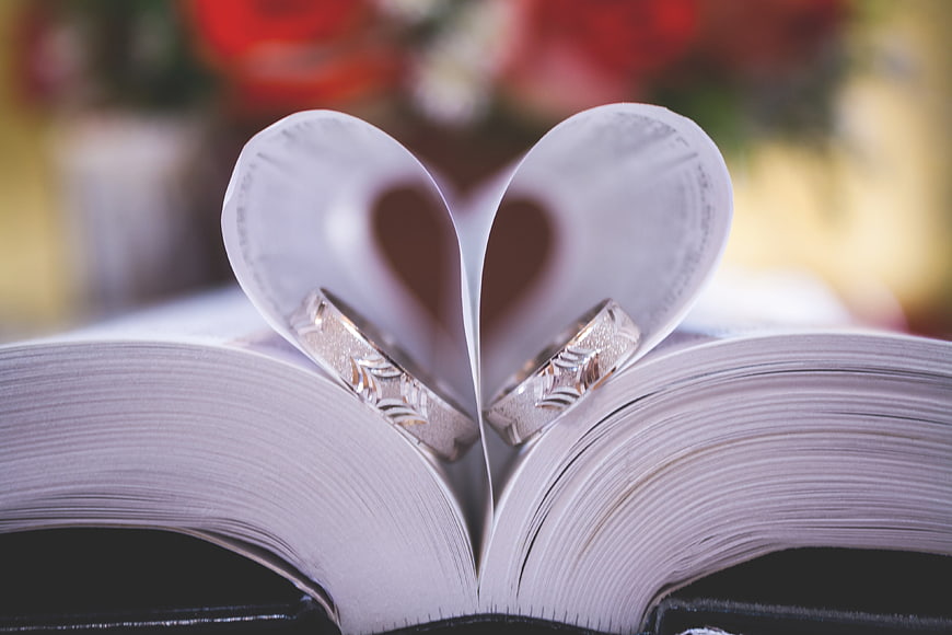 Wedding rings on open book pages folded into heart shape