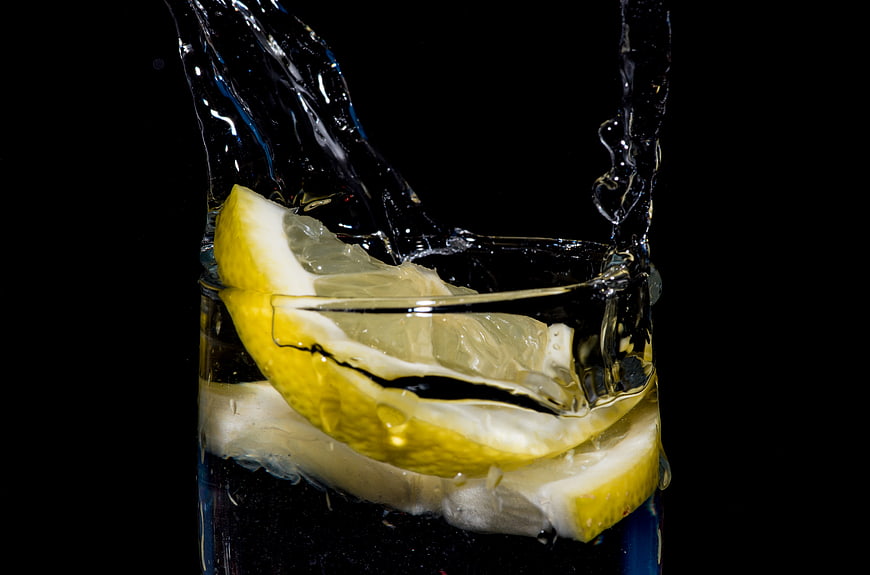 Refreshing lemon slices splashing in water on black background