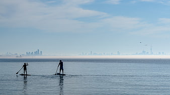Two paddleboarders silhouetted against a hazy city skyline