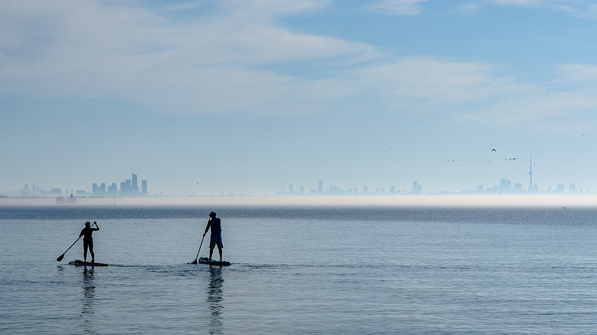 Two paddleboarders silhouetted against a hazy city skyline