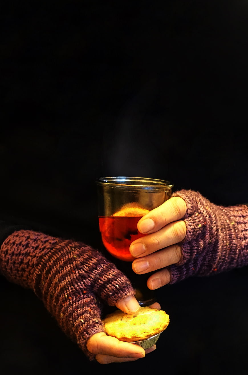 Hands holding mulled wine and mince pie in winter gloves