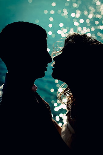 Silhouetted couple about to kiss against sparkling teal water background