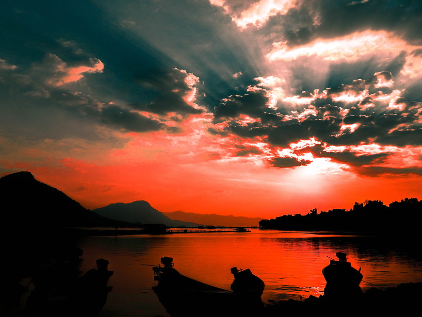 Dramatic sunset over lake with silhouetted boats and mountains