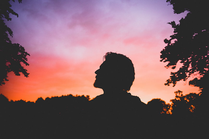 Silhouette of Man Looking Up at Colorful Sunset Sky