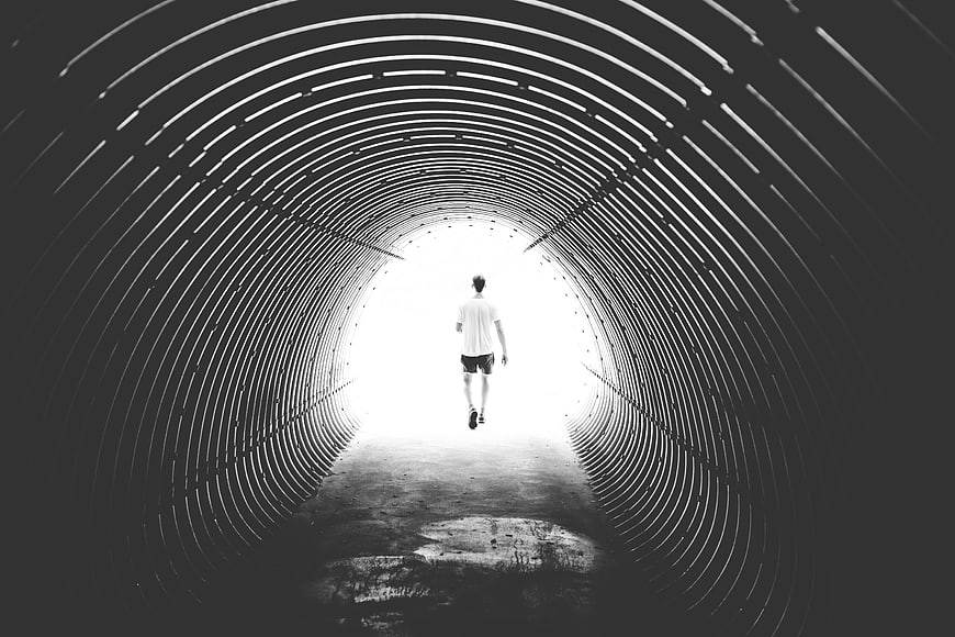 Man Walking Through Dark Tunnel Towards Bright Light