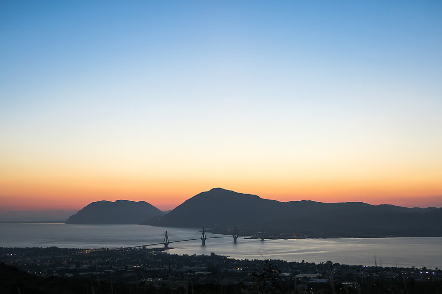 Sunset silhouette of suspension bridge and mountains over ocean