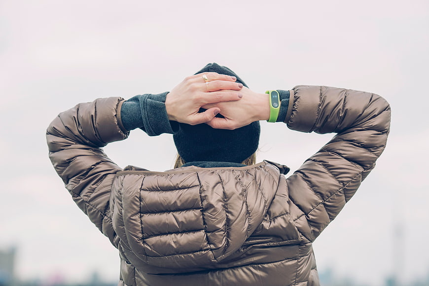Woman in brown puffer jacket with hands behind head
