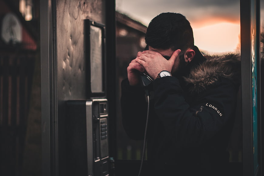 Man Covering Face in Phone Booth at Sunset