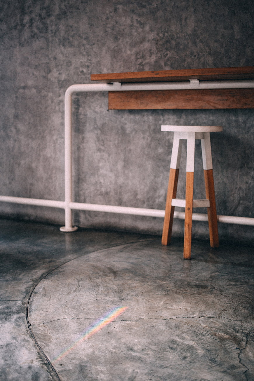 Minimalist industrial interior with wooden stool and rainbow light
