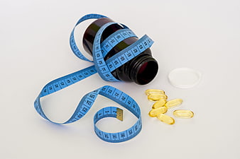 Blue measuring tape wrapped around dark bottle with yellow vitamin capsules