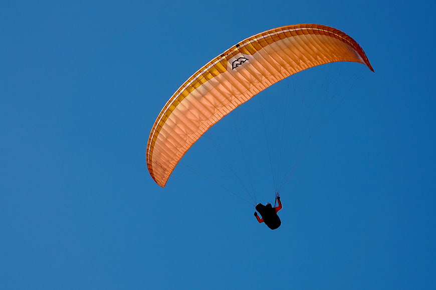 Orange Paraglider Flying Against Clear Blue Sky
