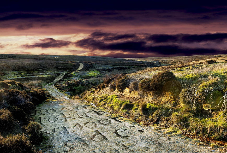 Dramatic moorland path with carved letters under stormy sunset sky