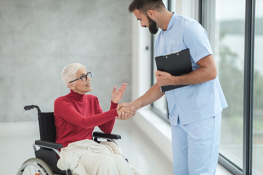 Male nurse shaking hands with elderly woman in wheelchair