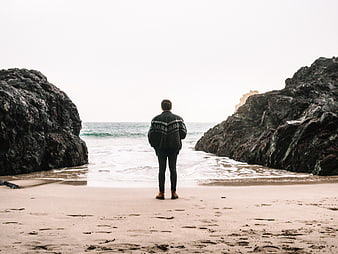 Man standing on beach looking at ocean between rocks