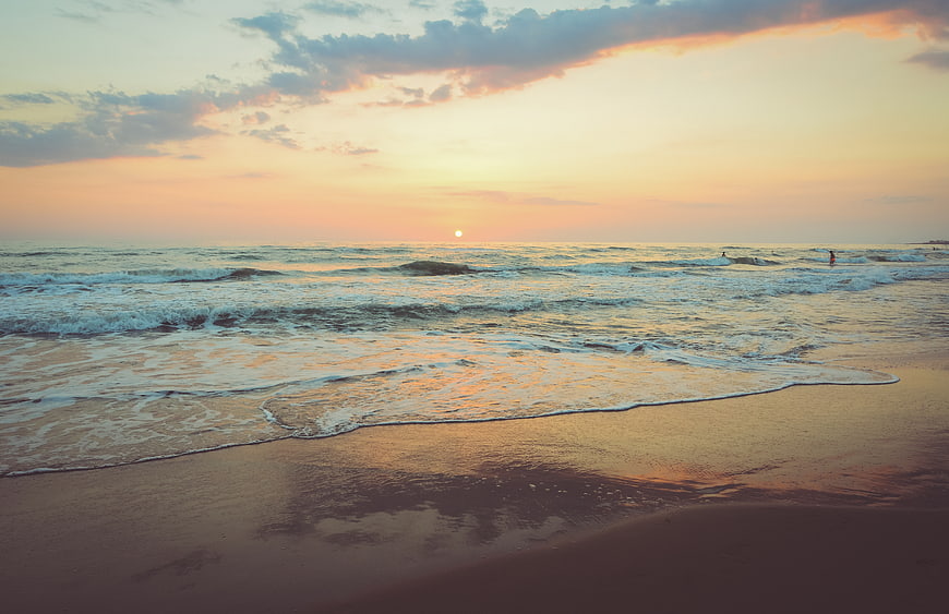 Serene Sunset Beach with Gentle Waves and Surfers