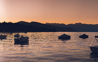 Silhouetted boats on a calm lake at sunset with mountains