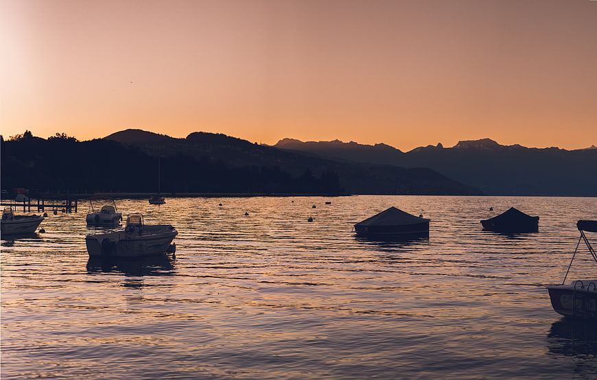Silhouetted boats on a calm lake at sunset with mountains