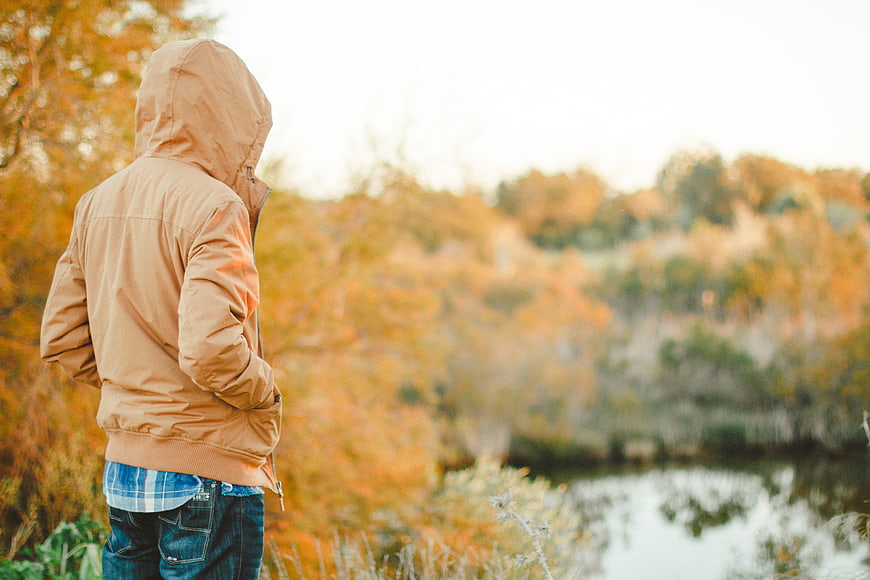 Man in Hooded Jacket Looking at Autumn Lake