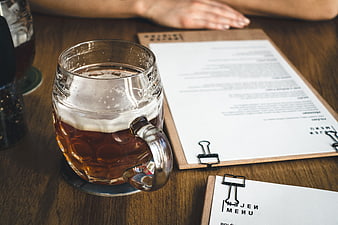 Glass mug of beer on wooden table with restaurant menu