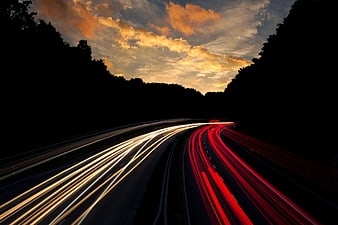 Long exposure highway light trails at sunset with dramatic clouds