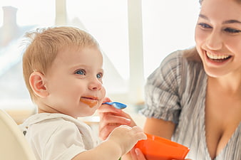 Mother Feeding Smiling Baby with Spoon Indoors