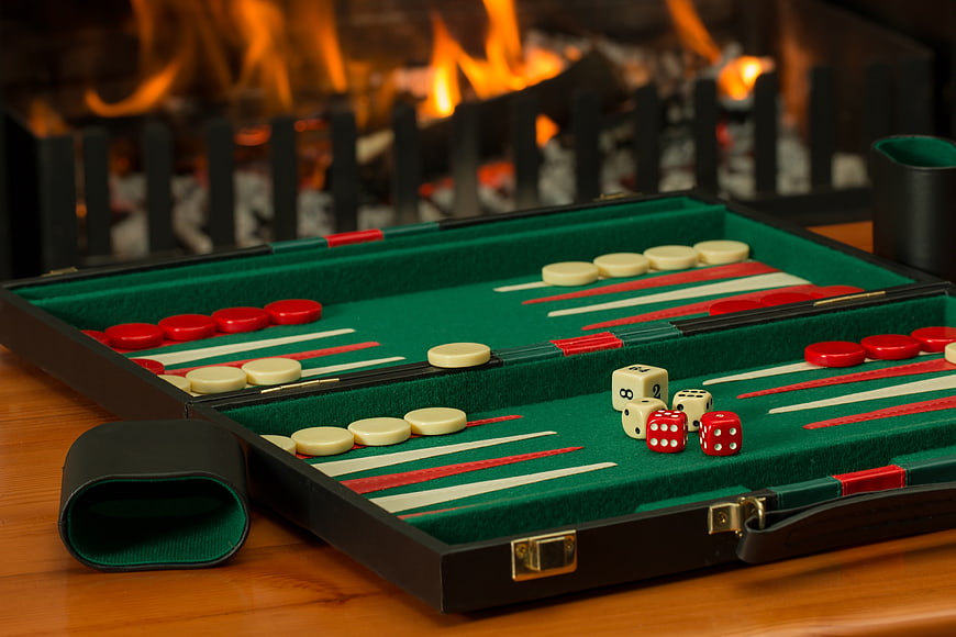 Backgammon board with dice and chips set against a warm fireplace background