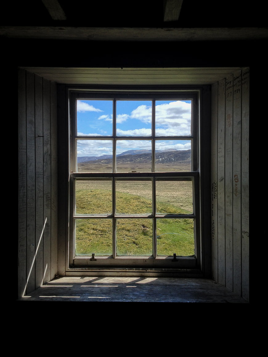 Rustic wooden window frame looking out onto a scenic Scottish countryside landscape